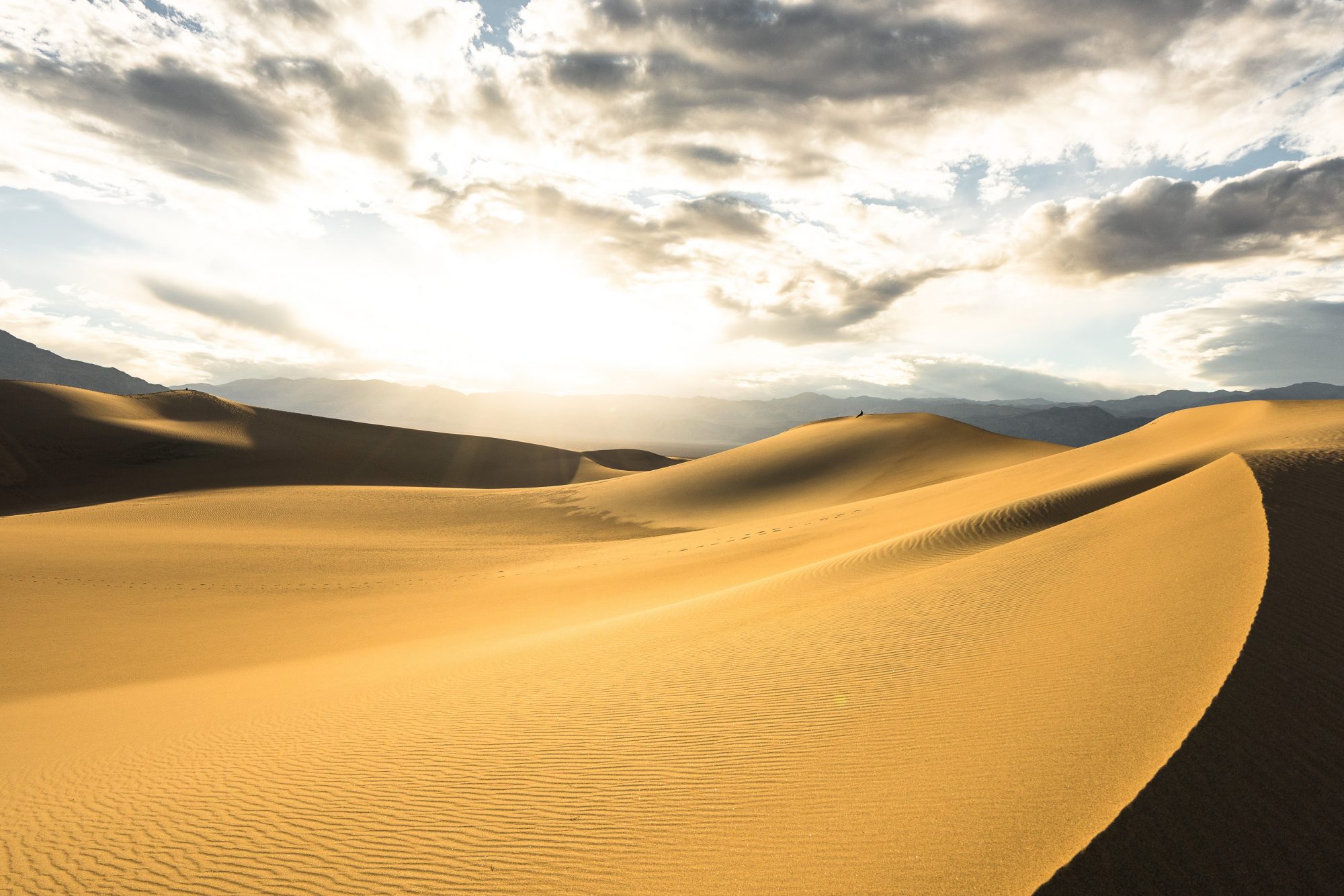a person sits and watches the sunset on the mesquite flat sand dunes in death valley national park | photo by jake landon schwartz