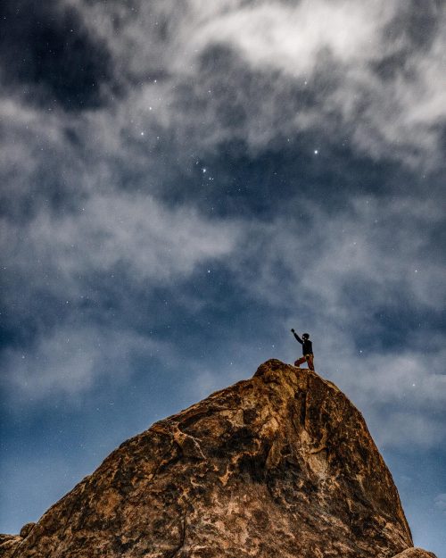 long exposure of man standing on top of a rock under a cloudy and starry sky in alabama hills california